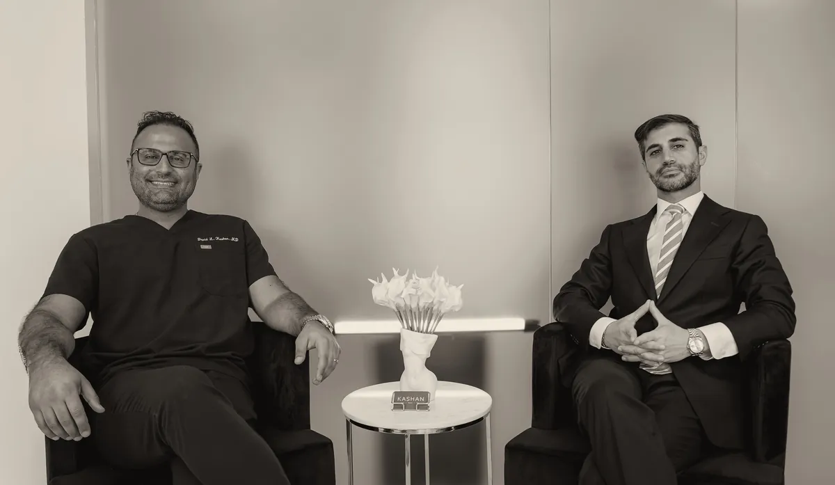 A Member's Hour conversation: a doctor in dark scrubs and a man in a suit, seated in armchairs either side of a small table