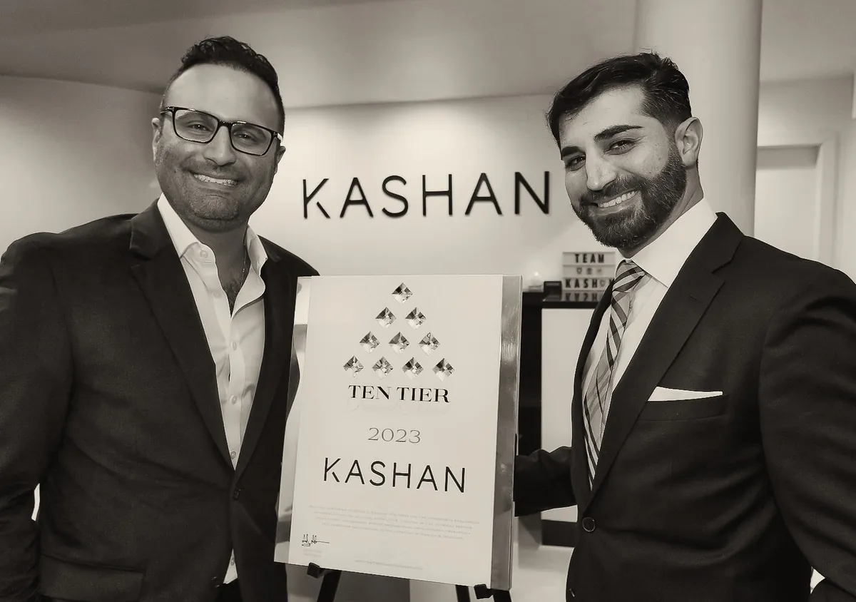 Two men in suits beside the 2023 Ten Tier Diamond Award for Kashan